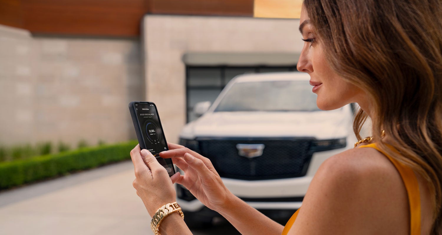 lady checking her mobile with a Cadillac vehicle background | Flow Cadillac in Winston Salem NC